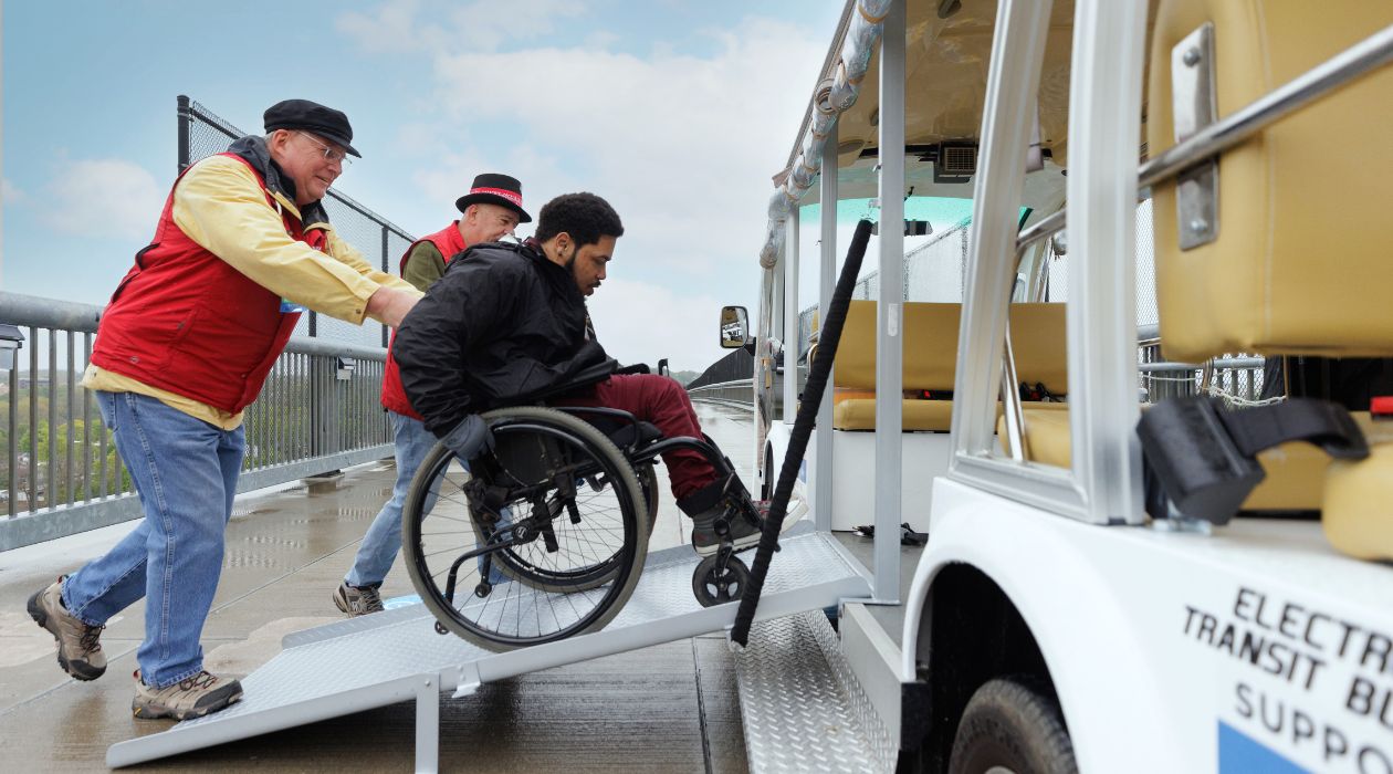 A wheelchair user is helped onto the electric tram by staff members at the Walkway Over the Hudson, Poughkeepsie